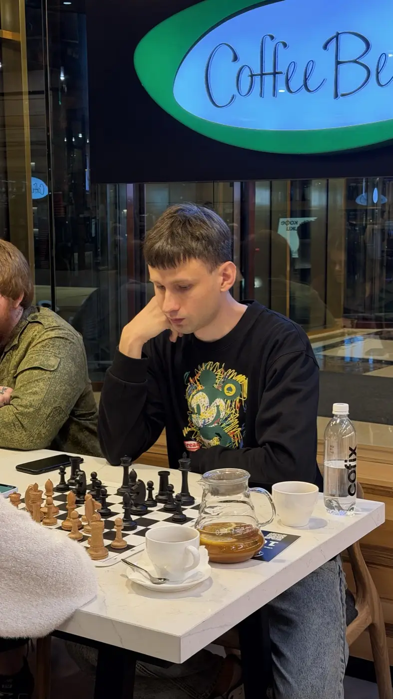 Молодой игрок над доской с деревянными фигурами, рядом чашка кофе