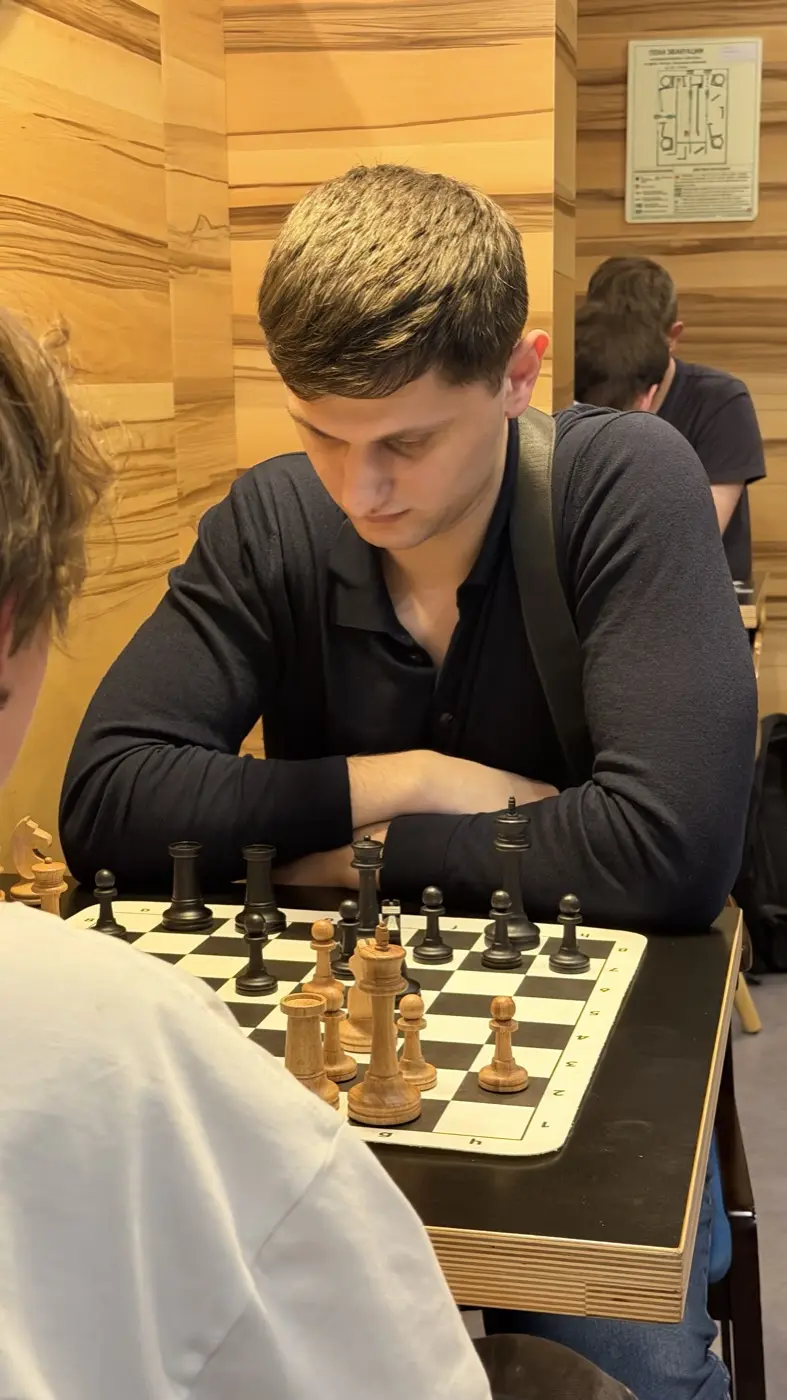 Игрок в тёмной рубашке над доской, скрестив руки