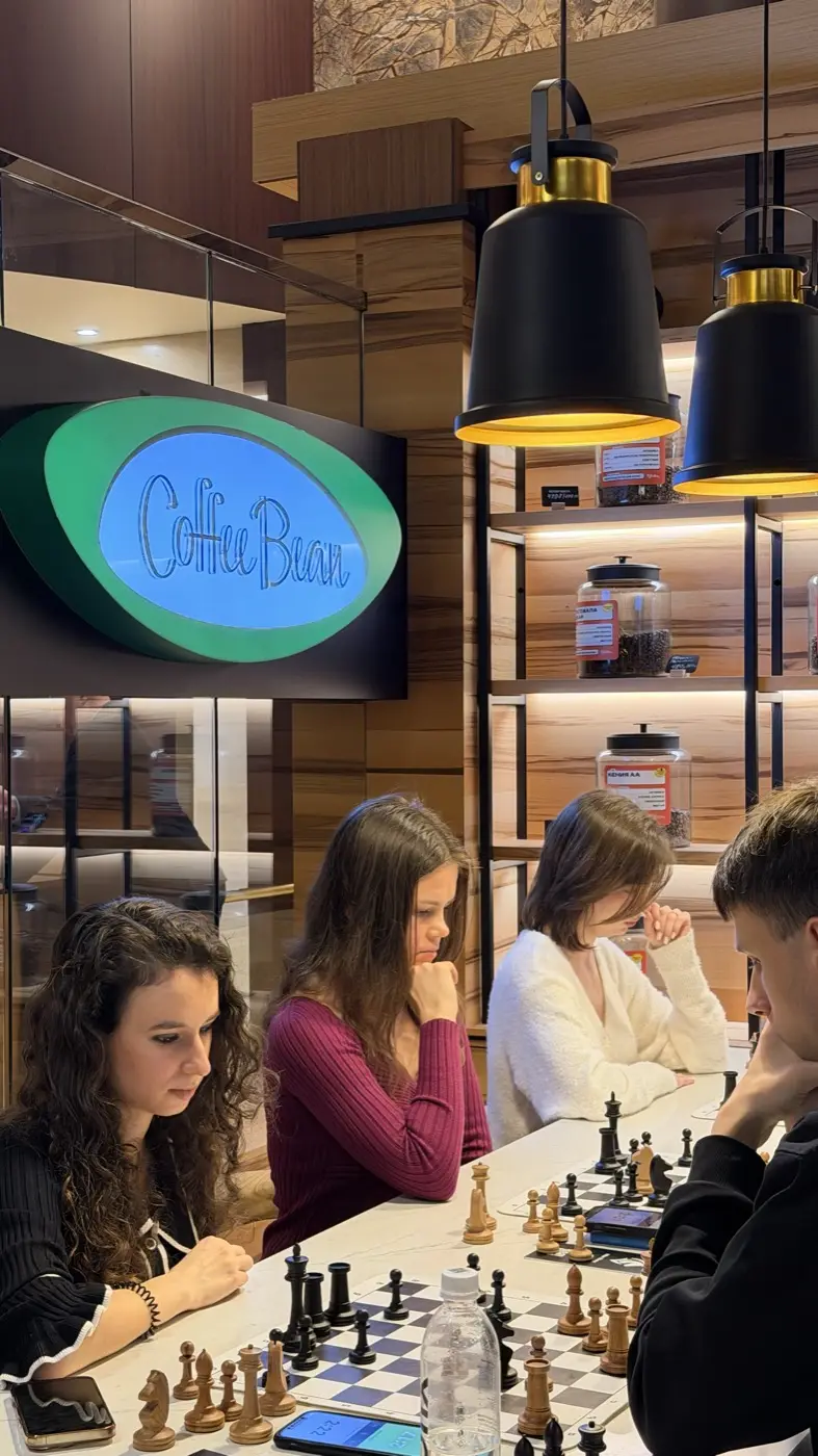 Три игрока за длинным столом под лампами, на стене вывеска Coffee Bean
